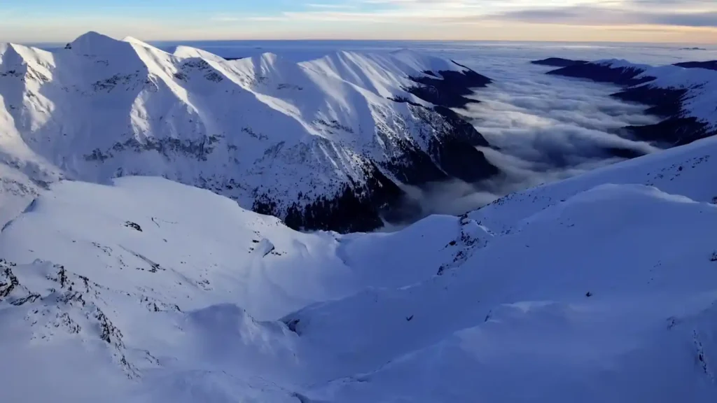 Snow-covered peaks of the Carpathian Mountains rising above a sea of clouds at sunset, showcasing the dramatic alpine landscape of Transylvania during winter