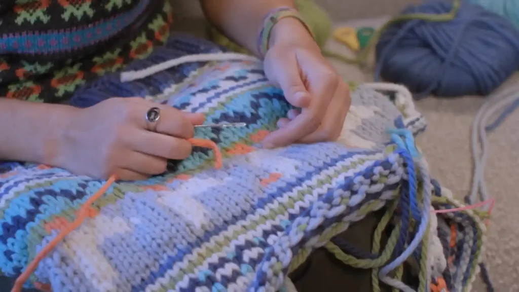 A contestant carefully works colorful wool threads using a crochet hook to create an intricate Fair Isle pattern during the first challenge of Game of Wool Britain's Best Knitter episode 1